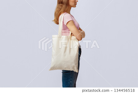Side View Shot Of Young Woman Carrying Blank Eco Tote Canvas Bag, Unrecognizable Millennial Lady Enjoying Sustainable Shopping, Standing Over Light Studio Background, Cropped Image, Copy Space 134456518