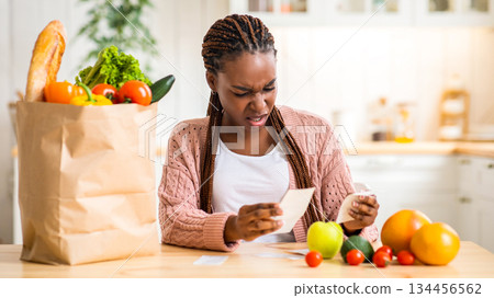 Expensive Groceries. Shocked African Housewife Sitting At Table In Kitchen, Checking Bills After Food Shopping In Supermarket, Frustrated Black Lady Dazed About Big Prices, Free Space 134456562