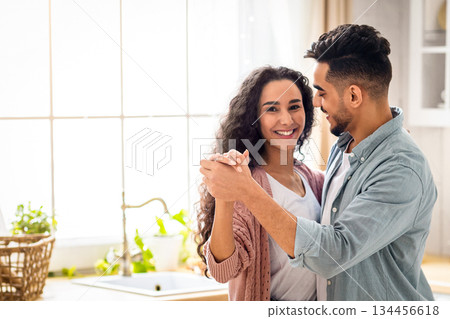 Romantic Moments. Portrait Of Happy Middle Eastern Spouses Dancing And Smiling In Kitchen, Modern Arab Family Having Fun At Home, Young Beautiful Couple Holding Hands And Bonding, Copy Space Romantic Moments. Portrait Of Happy Middle Eastern Spouses Dancing And Smiling In Kitchen, Modern Arab Family Having Fun At Home, Young Beautiful Couple Holding Hands And Bonding, Copy Space 134456618