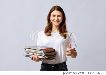 A woman showcases her commitment to recycling by holding a stack of magazines and giving a thumbs up. Her positive attitude highlights the importance of eco-friendly habits in daily life. A woman showcases her commitment to recycling by holding a stack of magazines and giving a thumbs up. Her positive attitude highlights the importance of eco-friendly habits in daily life. 134456630