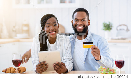 Portraif Of Happy Black Couple With Digital Tablet And Credit Card In Kitchen, Young African Spouses Making Food Or Groceries Delivery Order, Sitting At Table With Red Wine Glasses, Smiling At Camera Portraif Of Happy Black Couple With Digital Tablet And Credit Card In Kitchen, Young African Spouses Making Food Or Groceries Delivery Order, Sitting At Table With Red Wine Glasses, Smiling At Camera 134456634