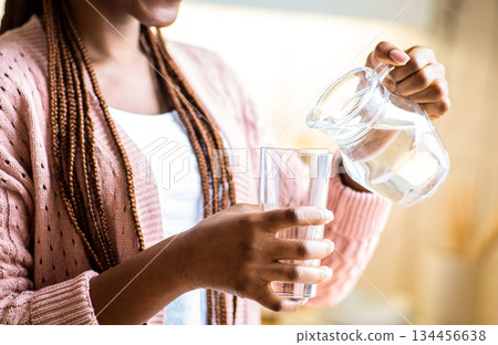 Smiling African American Woman Pouring Water From Jug To Glass. Unrecognizable Black Female Drinking Healthy Liquid In Kitchen, Enjoying Refreshing Drink, Cropped Image, Closeup Shot 134456638
