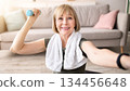 Joyful mature woman taking selfie while exercising with dumbbells at home. Happy senior lady making photo of herself during domestic strength workout, enjoying her training 134456648