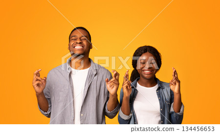 Make A Wish. Superstitious Black Couple Standing With Crossed Fingers And Closed Eyes, African American Man And Woman Pleading For Luck While Standing Together Isolated Over Yellow Background Make A Wish. Superstitious Black Couple Standing With Crossed Fingers And Closed Eyes, African American Man And Woman Pleading For Luck While Standing Together Isolated Over Yellow Background 134456653