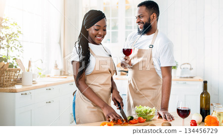 Aperitif Drink. Happy Black Spouses Drinking Red Wine While Cooking Food In Kitchen, Loving Young African American Couple Preparing Healthy Lunch Together And Having Fun At Home, Free Space 134456729