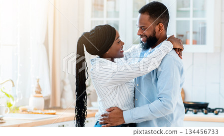 Portrait Of Young Happy Black Man And Woman Ebracing In Kitchen While Having Date At Home, Romantic African American Couple Dancing And Smiling To Each Other, Enjoying Time Together, Side View 134456733