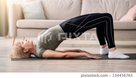 Stay at home fitness. Strong mature woman doing half bridge yoga pose, strengthening her abs muscles indoors, copy space. Fit senior woman working out in living room during covid isolation Stay at home fitness. Strong mature woman doing half bridge yoga pose, strengthening her abs muscles indoors, copy space. Fit senior woman working out in living room during covid isolation 134456765