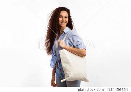 Cheerful Woman With White Eco Bag Smiling To Camera Posing Standing Over White Studio Background. Female Consumer Carrying Flax Tote Shopper Handbag. Eco-Friendly Lifestyle, Stop Using Plastic Concept Cheerful Woman With White Eco Bag Smiling To Camera Posing Standing Over White Studio Background. Female Consumer Carrying Flax Tote Shopper Handbag. Eco-Friendly Lifestyle, Stop Using Plastic Concept 134456864