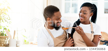 Joyful Young Black Spouses Tasting Food While Cooking Lunch In Kitchen, Happy African American Family Preparing Food At Home And Drinking Wine, Enjoying Spending Time Together, Copy Space 134456868