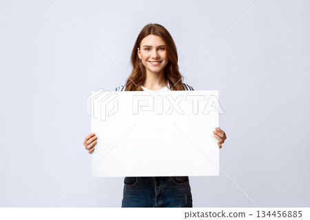 Smiling Millennial Lady Holding Blank Placard With Copy Space For Advertisement. Positive Young Woman Showing Empty Poster With Free Place For Your Text Or Design, Standing On Light Studio Background 134456885