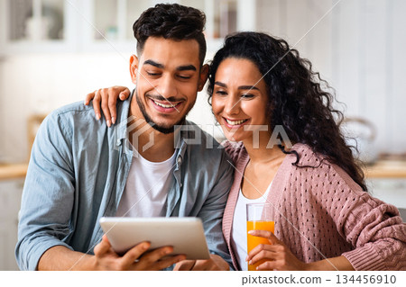 Morning Leisure. Young Happy Arab Spouses Eating Breakfast And Using Digital Tablet In Kitchen, Cheerful Middle Eastern Lovers Spending Time With Tab Computer And Enjoying Tasty Food, Closeup 134456910