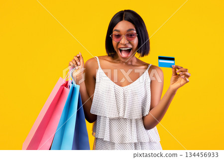 Summertime sales concept. Excited black woman with shopping bags showing credit card, shouting OMG on orange studio background. Overjoyed young lady using electronic money, paying contactless Summertime sales concept. Excited black woman with shopping bags showing credit card, shouting OMG on orange studio background. Overjoyed young lady using electronic money, paying contactless 134456933