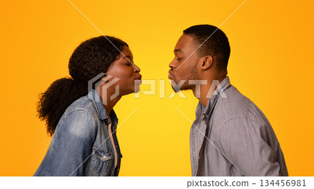 First Kiss. Side view of romantic black man and woman reaching out each other for kissing over yellow studio background, young african american lovers having tender moments, free space 134456981