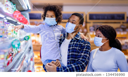 Grocery shopping during coronavirus pandemic. Millennial black family wearing protective masks while shopping for milk products at dairy section of modern supermarket Grocery shopping during coronavirus pandemic. Millennial black family wearing protective masks while shopping for milk products at dairy section of modern supermarket 134456990