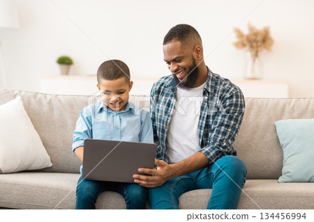 African American Father Teaching Son To Use Laptop Browsing Internet At Home. Little Boy And His Dad Browsing Internet Or Watching Movie Online Together On Weekend. Modern Gadgets Lifestyle 134456994