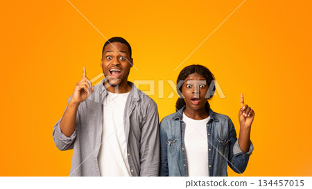 Idea Concept. Exciyed African American Couple Pointing Fingers Up While Standing Isolated Over Yellow Background, Inspired Emotional Black Man And Woman Found Problem Solution, Copy Space 134457015