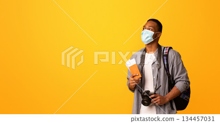 New Travel Rules. Young Black Tourist Man In Medical Face Mask Looking Aside At Copy Space, African Guy With Passport And Photo Camera Ready For Trip During Coronavirus Pandemic, Yellow Background 134457031