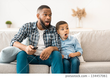 Television Programming Problem. Shocked African Father And Son Watching Questionable Content On TV Together Sitting On Couch With Opened Mouth At Home. Parental Control Concept 134457061