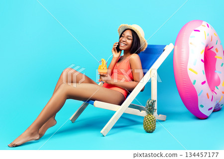 Sweet black woman in swimsuit enjoying summer cocktail, speaking on smartphone over blue studio background, panorama with copy space. Young lady having phone conversation and refreshing drink Sweet black woman in swimsuit enjoying summer cocktail, speaking on smartphone over blue studio background, panorama with copy space. Young lady having phone conversation and refreshing drink 134457177