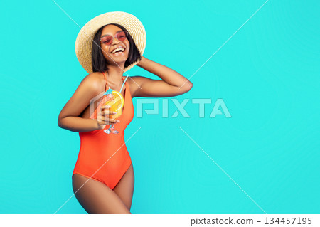 Fit black lady in straw hat and swimsuit posing with tropical fruit cocktail on summer vacation, blue studio background. Smiling young woman in bikini having fresh drink, enjoying beach party Fit black lady in straw hat and swimsuit posing with tropical fruit cocktail on summer vacation, blue studio background. Smiling young woman in bikini having fresh drink, enjoying beach party 134457195