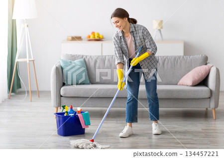 Full length portrait of happy young woman wiping floor in living room, copy space. Millennial housewife cleaning her apartment, doing household duties, practising hygiene, keeping her home tidy Full length portrait of happy young woman wiping floor in living room, copy space. Millennial housewife cleaning her apartment, doing household duties, practising hygiene, keeping her home tidy 134457221