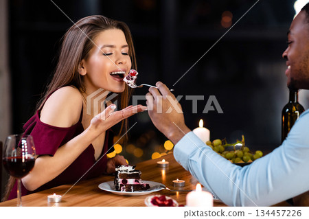 Try it. Cheerful mixed couple feeding each other with dessert, having fun at romantic date in restaurant, elegant multiracial lovers enjoying celebrating valentine's day or anniversary together 134457226