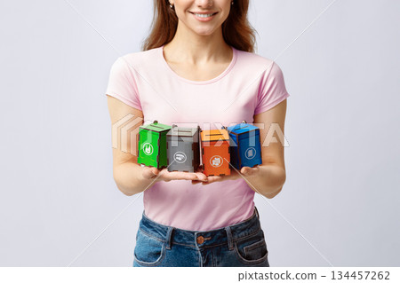 Concept Image For Waste Sorting With Young Woman Holding Different Colorful Toy Garbage Containers For Different Kind Of Trash, Standing Over Gray Background In Studio, Cropped Image, Closeup 134457262