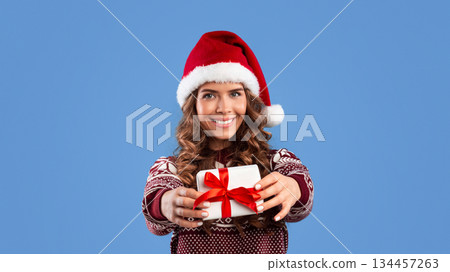 Sexy young woman in Santa hat and woolen sweater showing Christmas gift on blue background, panorama Sexy young woman in Santa hat and woolen sweater showing Christmas gift on blue background, panorama 134457263