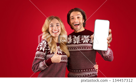 Hapy millennial couple in Christmas sweaters showing thumb up and peace gestures over red background 134457312