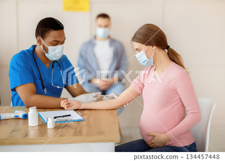 African American doctor giving Covid-19 vaccine injection to young pregnant woman at health centre. Expectant lady being immunized against coronavirus at clinic. Population vaccination concept 134457448