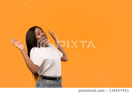 Excited young black woman raising hands up, standing by copy space for text or advertisement, orange studio background. Amazed african american lady and empty space for advertising Excited young black woman raising hands up, standing by copy space for text or advertisement, orange studio background. Amazed african american lady and empty space for advertising 134457451