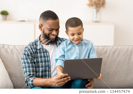 Little Boy Watching Movie On Tablet Sitting On Dad's Knees, Using Computer Together And Browsing Internet At Home. Gadgets, Weekend Family Leisure Concept 134457474