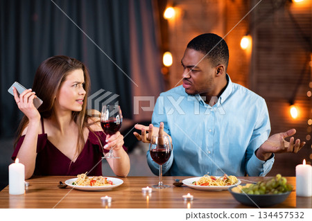 Annoyed Black Guy Arguing With His Girlfriend Busy With Cellphone On Date In Restaurant. Young Multiracial Couple Having Problems In Relationship During Romantic Dinner At Valentine's Day, Free Space 134457532