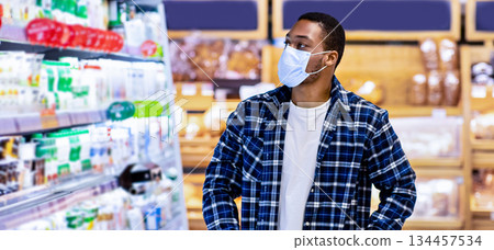 Young black guy in disposable face mask selecting dairy products at store during covid quarantine. African American man shopping for fresh food products at mall or supermarket Young black guy in disposable face mask selecting dairy products at store during covid quarantine. African American man shopping for fresh food products at mall or supermarket 134457534