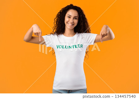 Cheerful Volunteer Lady Pointing Fingers Down Smiling To Camera Posing Standing Over Yellow Studio Background. Activist Advertising Something. Look There, Volunteering Advertisement 134457540