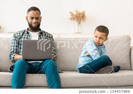 Indifferent African Father Using Laptop Ignoring Offended Son Sitting On Sofa At Home. Family Problems, Bad Relationship, Busy Dad Neglecting His Kid Concept Indifferent African Father Using Laptop Ignoring Offended Son Sitting On Sofa At Home. Family Problems, Bad Relationship, Busy Dad Neglecting His Kid Concept 134457969