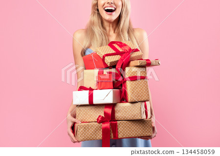 Excited young lady holding stack of holiday gifts on pink studio background. Cheerful millennial woman with pile of festive presents. Birthday, Woman's Day, Valentine celebration concept Excited young lady holding stack of holiday gifts on pink studio background. Cheerful millennial woman with pile of festive presents. Birthday, Woman's Day, Valentine celebration concept 134458059
