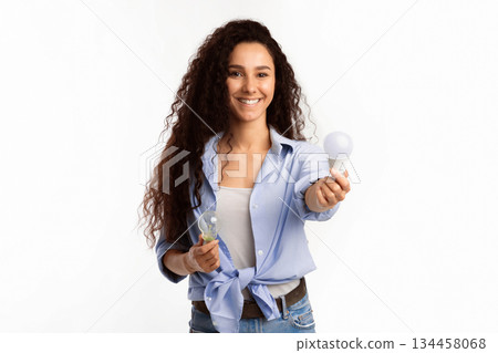 Smiling Lady Showing Compact Fluorescent Lamp Light Bulb To Camera Standing Over White Studio Background. Lightbulbs Disposal Service, Choose Energy-Saving Light-Bulb Concept Smiling Lady Showing Compact Fluorescent Lamp Light Bulb To Camera Standing Over White Studio Background. Lightbulbs Disposal Service, Choose Energy-Saving Light-Bulb Concept 134458068