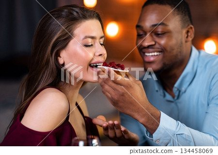 Cheerful Interracial Couple Enjoying Sharing Dessert Together During Romantic Date In Restaurant, Loving African American Man Feeding His Happy Girfriend, Multicultural Lovers Enjoying Dinner Cheerful Interracial Couple Enjoying Sharing Dessert Together During Romantic Date In Restaurant, Loving African American Man Feeding His Happy Girfriend, Multicultural Lovers Enjoying Dinner 134458069