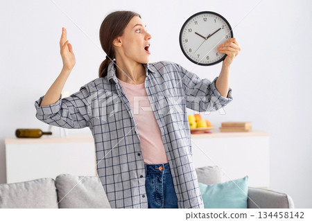 Shocked young woman holding clock, feeling terrified, standing in messy room after party, being late to clean apartment, copy space. Millennial maid not meeting cleanup deadline Shocked young woman holding clock, feeling terrified, standing in messy room after party, being late to clean apartment, copy space. Millennial maid not meeting cleanup deadline 134458142