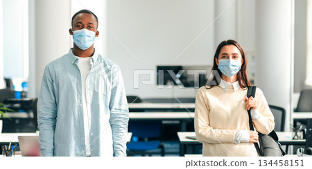 New Normal And Epidemic Concept. Portrait of international students wearing protective medical masks, standing indoors, and posing. Young woman and african american man looking at camera 134458151