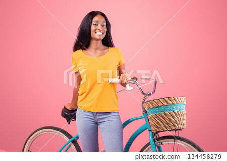 Full length portraif of pretty black lady with vintage bicycle smiling at camera on pink studio background. Positive African American woman going cycling, loving adventure and active sports 134458279