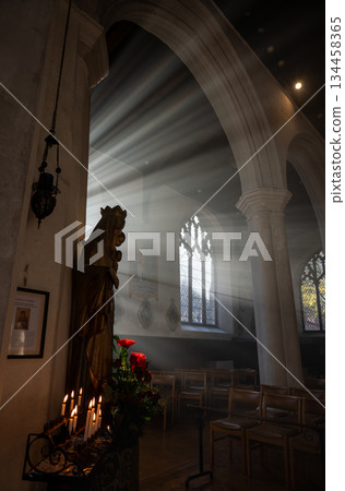 Norwich, Norfolk, UK: Church interior with a statue of Mary and Jesus. Sunlight streams through the windows. Candles and flowers complete the scene. 134458365