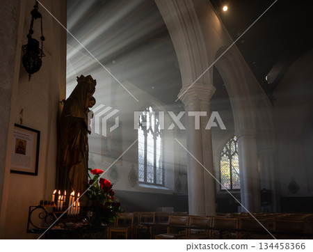 Norwich, Norfolk, UK: Church interior with a statue of Mary and Jesus. Sunlight streams through the windows. Candles and flowers complete the scene. 134458366