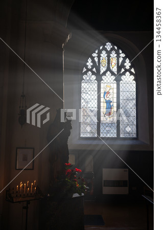 Norwich, Norfolk, UK: Church interior with a statue of Mary and Jesus. Sunlight streams through the window. Candles and flowers complete the scene. Norwich, Norfolk, UK: Church interior with a statue of Mary and Jesus. Sunlight streams through the window. Candles and flowers complete the scene. 134458367