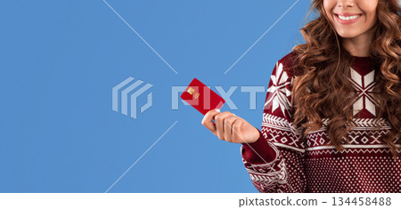 Online shopping for Christmas. Pretty girl in Santa hat holding smartphone and credit card on blue background, panorama 134458488