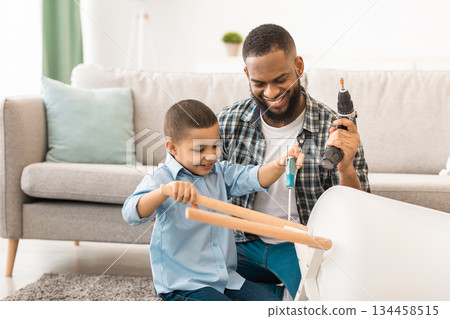 Happy African Little Boy Helping Father Fix Table Doing Housework Chores Together Sitting On Floor At Home. Household Work For Children Concept. Selective Focus 134458515