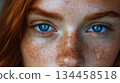 A womans intense blue eyes and freckled features fill the frame in a close-up portrait. A womans intense blue eyes and freckled features fill the frame in a close-up portrait. 134458518