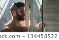 A man with a well-kept beard grooming himself next to a glass shower panel in a bathroom filled with natural light. A man with a well-kept beard grooming himself next to a glass shower panel in a bathroom filled with natural light. 134458522
