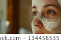 A woman gazes into the distance while wearing a white facial beauty mask in a well-lit room. A woman gazes into the distance while wearing a white facial beauty mask in a well-lit room. 134458535